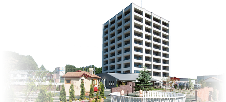 介護施設の建物外観と周辺環境。複数階の新築建物と庭園が見える。
